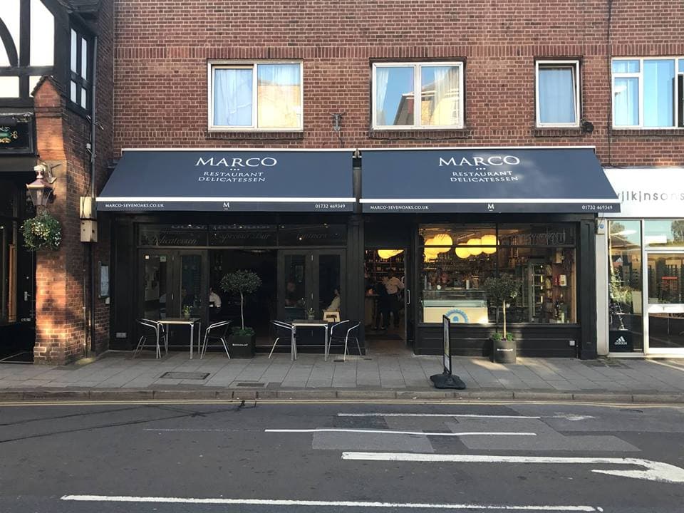 The Marco shopfront on Sevenoaks High Street — navy awnings, outdoor seating with potted bay trees, and the Italian Restaurant + Delicatessen wordmark