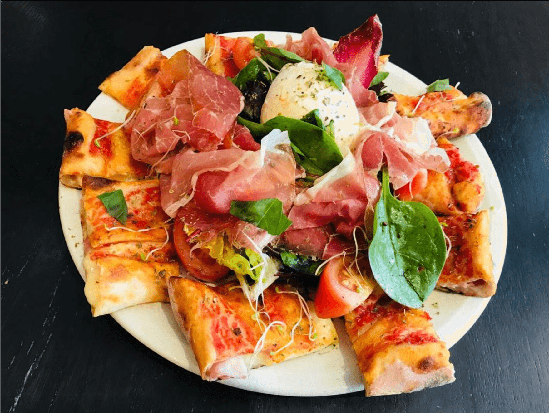 Italian antipasto sharing platter — burrata, Parma ham and rocket over fresh tomato and greens, framed by triangular pizza-bread wedges