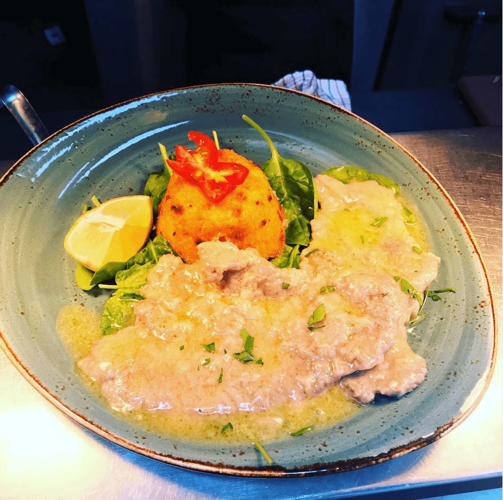 Pollo Milanese — breaded chicken in a lemon butter sauce with an arancini ball and lemon on a bed of fresh leaves